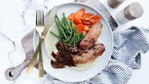 Bangers in bacon with mash, caramelised onion gravy & veggies recipe