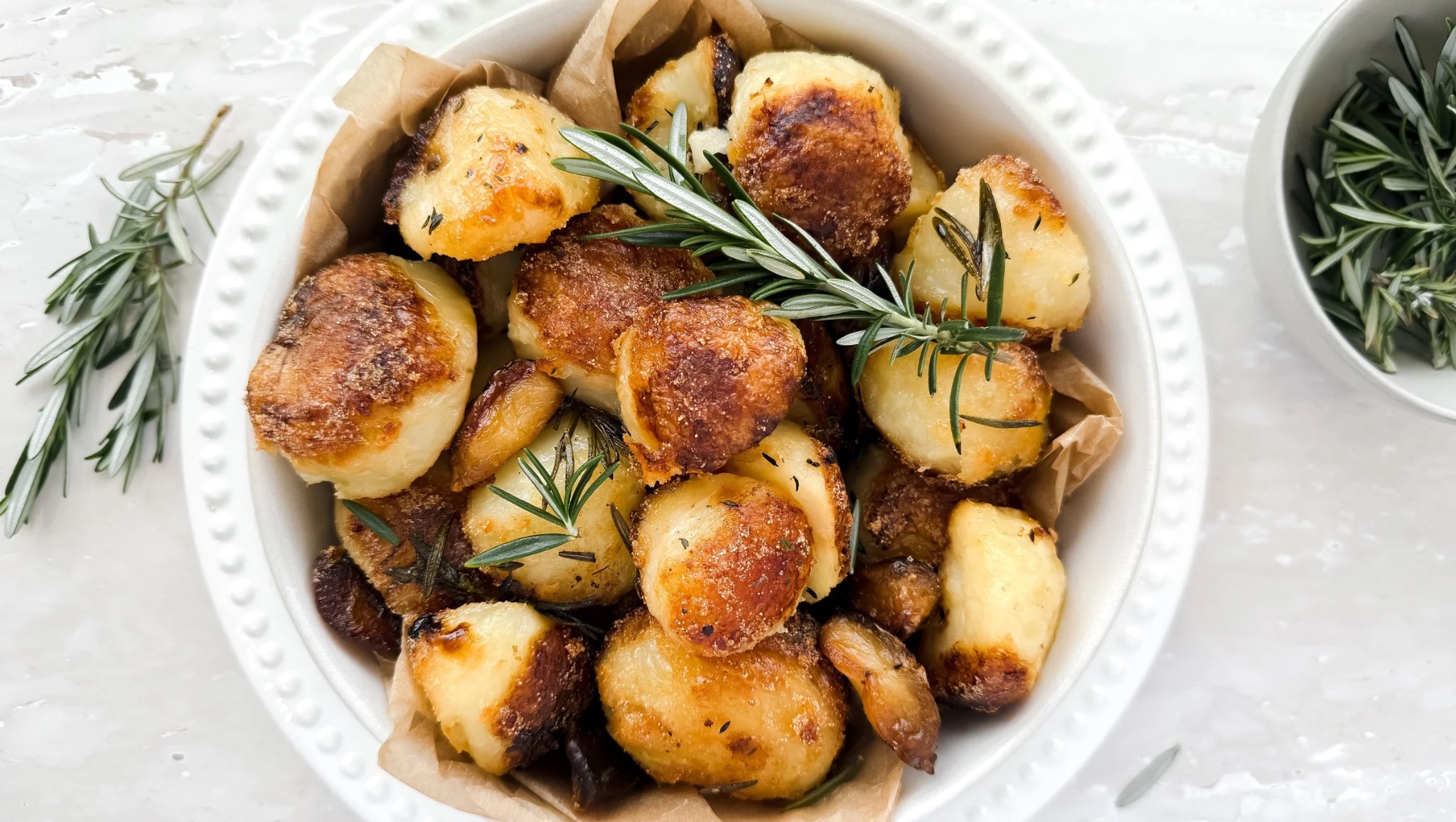 Crispy duck fat roasted potatoes with golden edges, seasoned with garlic and fresh herbs on a serving platter.