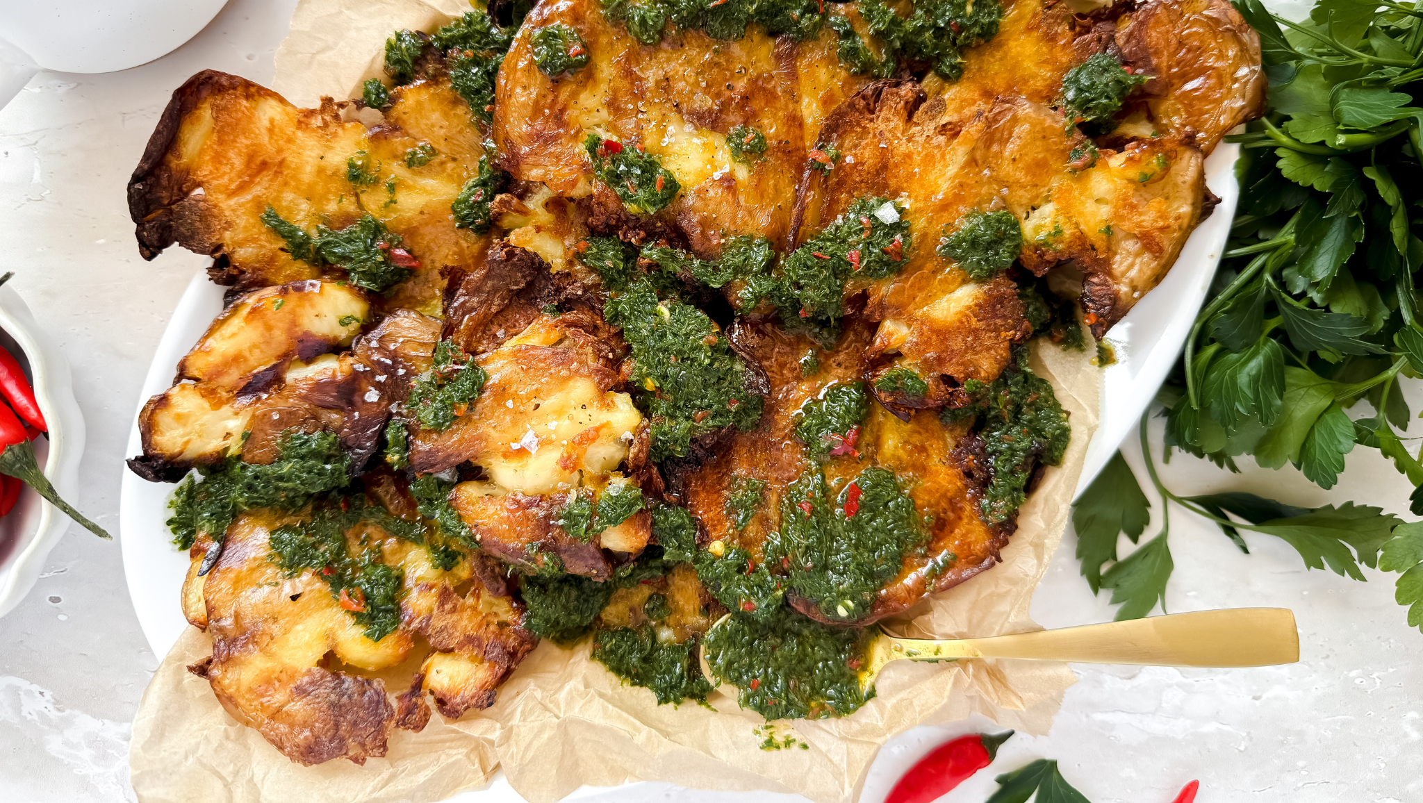 Crispy smashed potatoes topped with chimichurri sauce, served on a platter with creamy hummus dip.